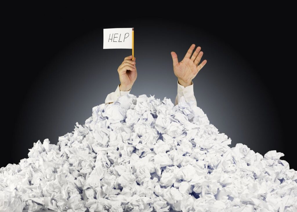 Person under crumpled pile of papers with hand holding a help sign